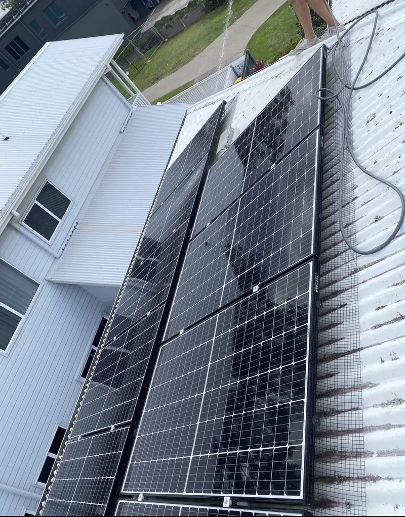 Solar panel bird proofing in Albany Creek: Installer hosing solar panels edged with black mesh on a white corrugated metal roof