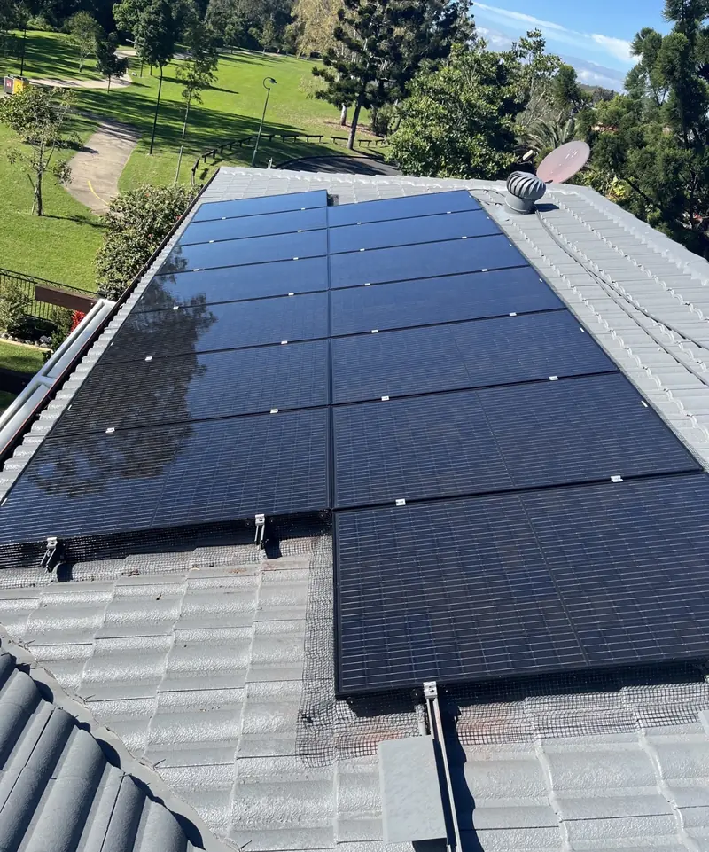 Solar panel bird proofing in Calamvale: Black solar array with mesh skirting on a grey tile roof overlooking green parkland
