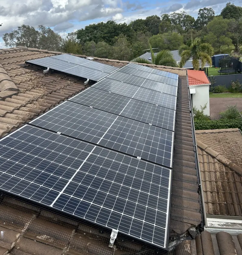 Solar panel bird proofing in Capalaba: Rows of solar panels with black edge mesh on a weathered brown tile roof, backyard below