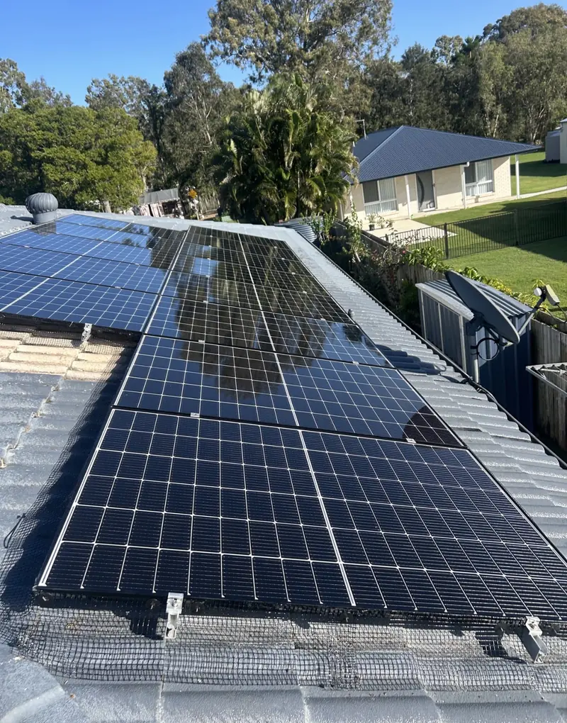 Solar panel bird proofing in Carindale: Black solar panels skirted with bird mesh on a pale grey tile roof, satellite dish nearby