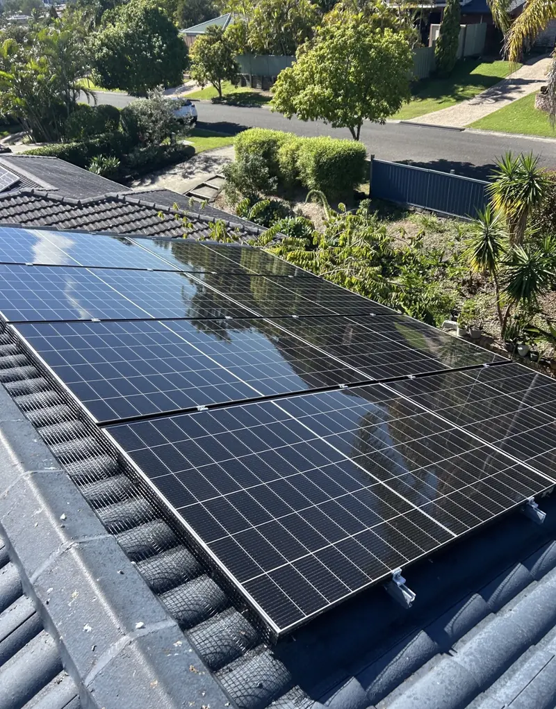 Solar panel bird proofing in Deception Bay: Meshed solar array on a charcoal tile roof with suburban street and gardens beyond