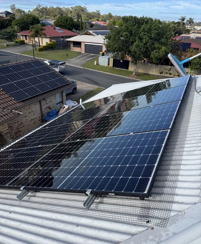 Solar panel bird proofing in Hemmant: Black mesh secured around solar panels on a white corrugated metal roof, cleaning brush resting nearby