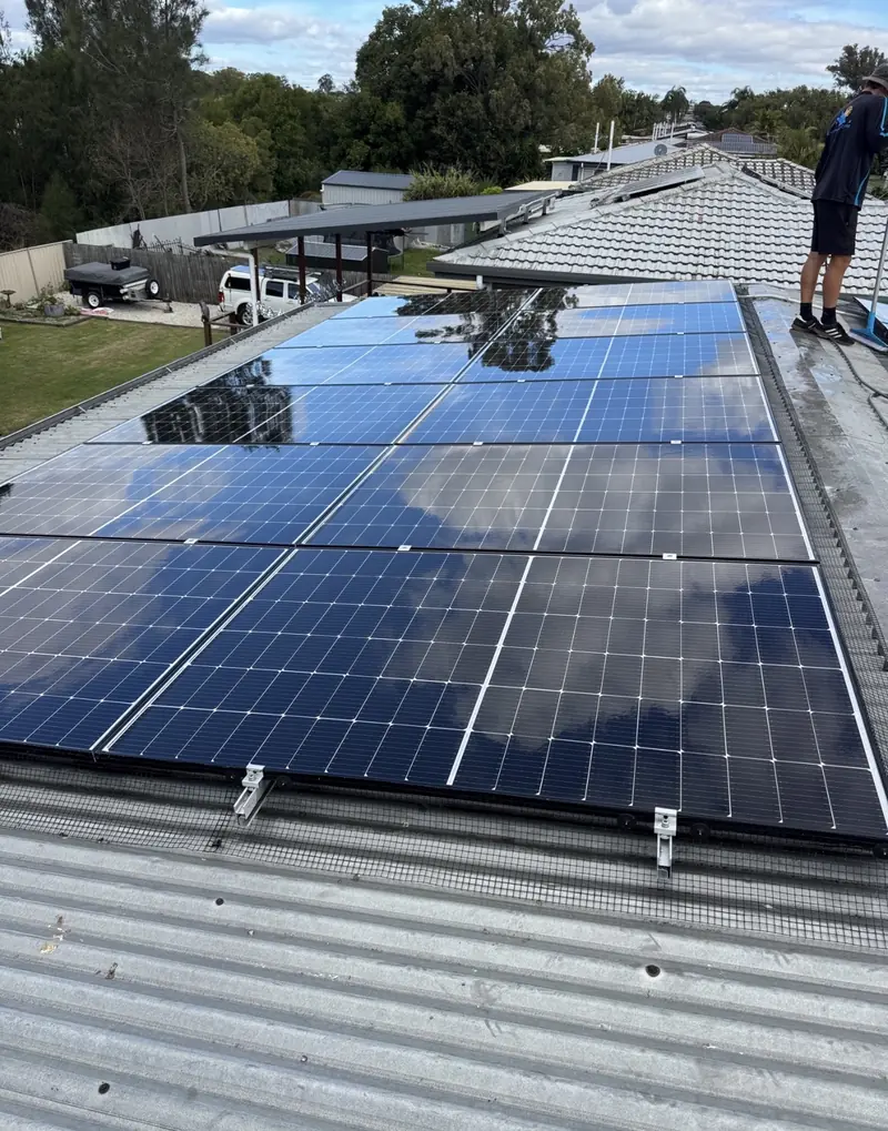Solar panel bird proofing in Kedron: Installer standing beside a meshed solar array on a grey corrugated metal roof, clouds reflected