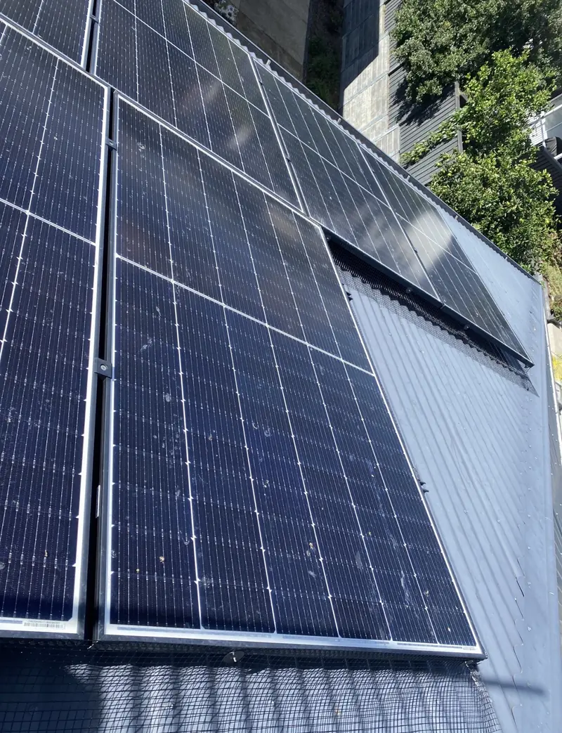 Solar panel bird proofing in Kenmore: Close-up of bird mesh fitted beneath solar panel edges on a dark blue-grey metal roof