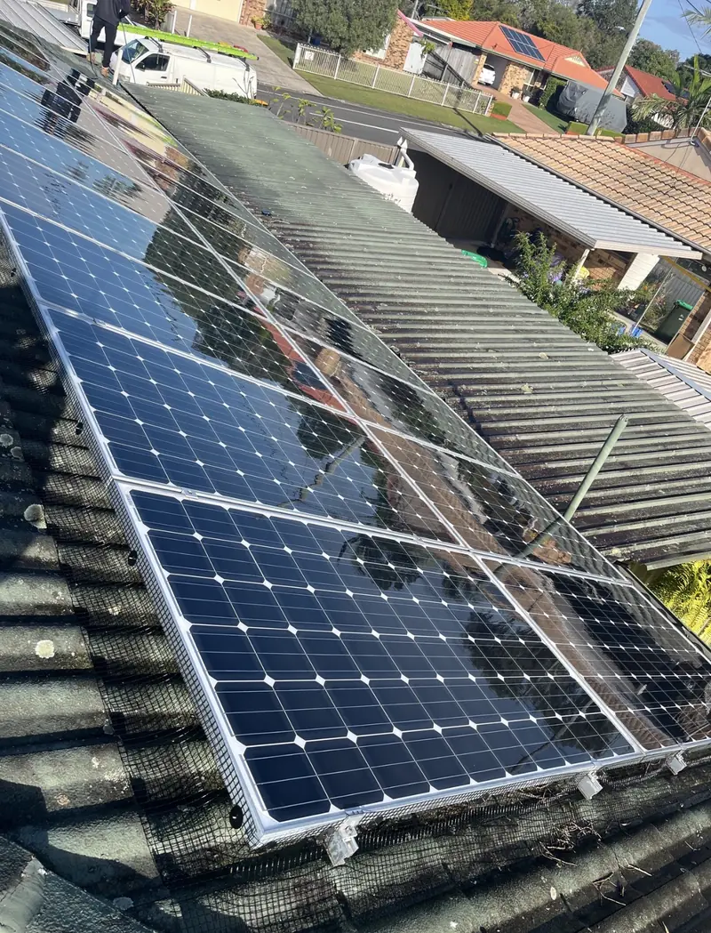 Solar panel bird proofing in Logan: Mesh installed around solar panels on an aged green corrugated roof, work van parked below