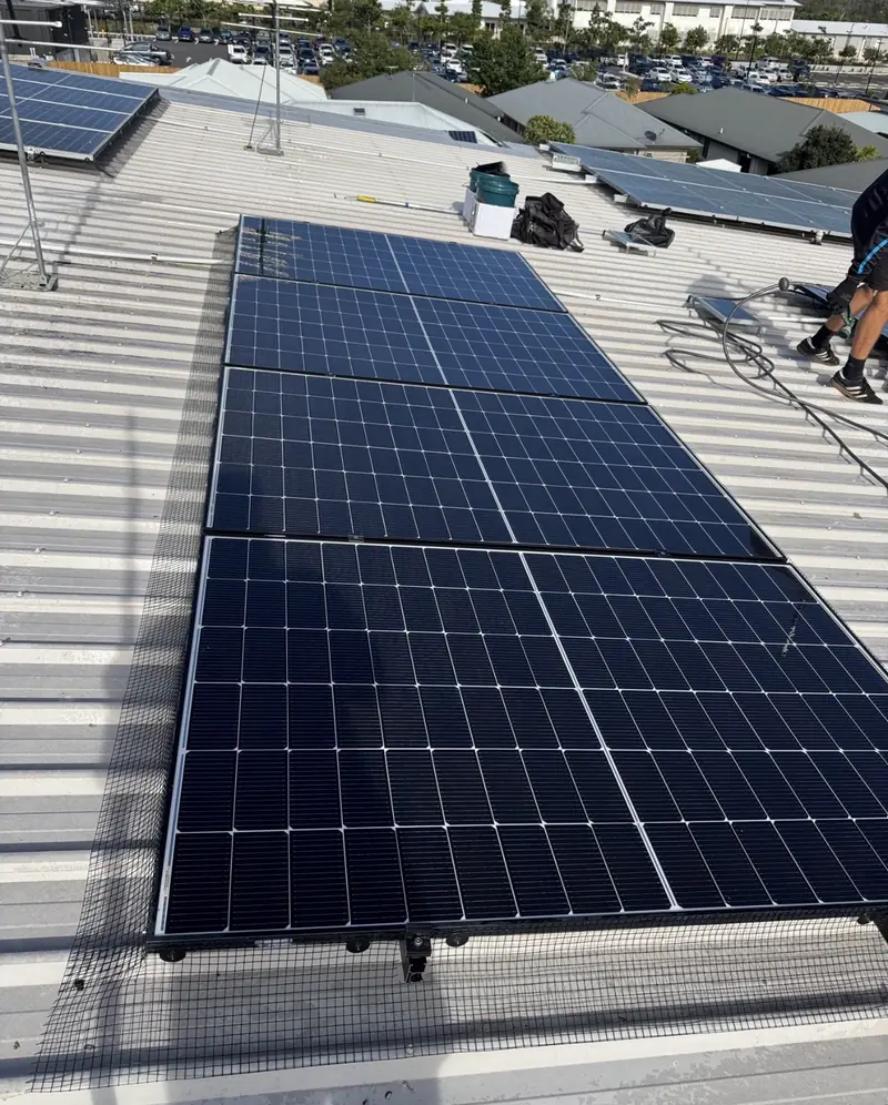 Solar panel bird proofing in Loganholme: Mesh skirt around a solar array on a low-pitch commercial metal roof, car park behind