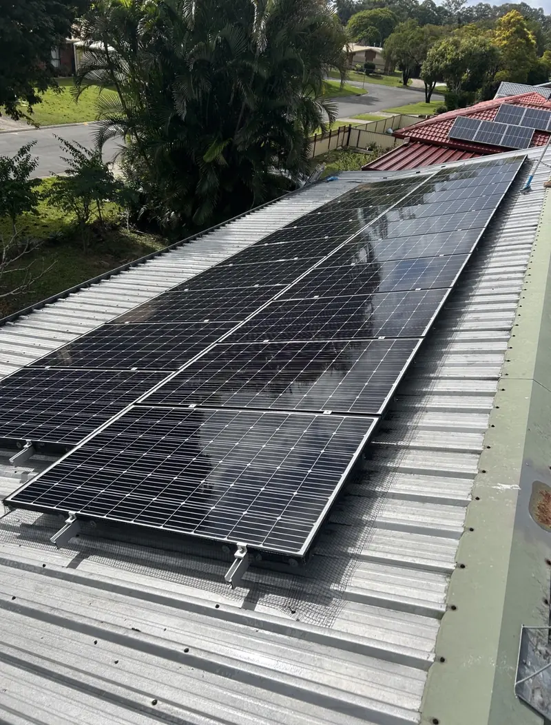 Solar panel bird proofing in Lota: Long solar array with wire mesh skirts on a silver corrugated metal roof beside houses