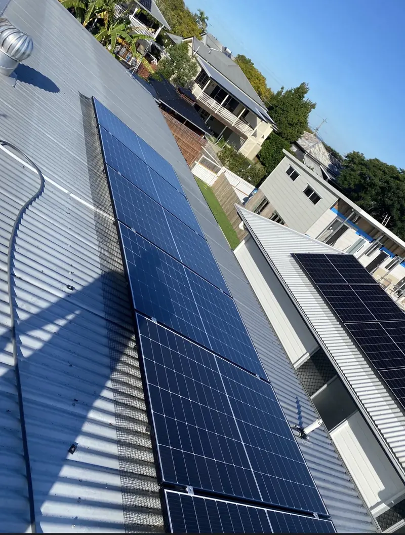 Solar panel bird proofing in Mount Gravatt: Meshed solar panels and a whirlybird vent on a silver corrugated roof, two-storey homes behind
