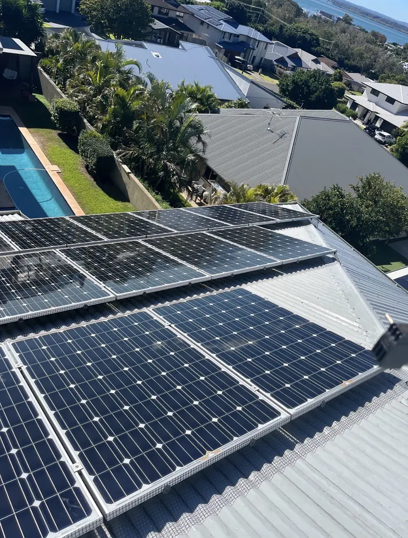Solar panel bird proofing in Nundah: Older silver-framed solar panels with mesh skirts on a metal roof above a lap pool