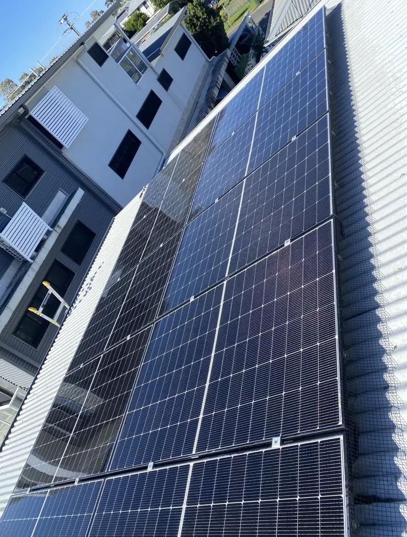 Solar panel bird proofing in Redcliffe: Black-framed solar panels with edge mesh on a silver corrugated metal roof beside two-storey houses