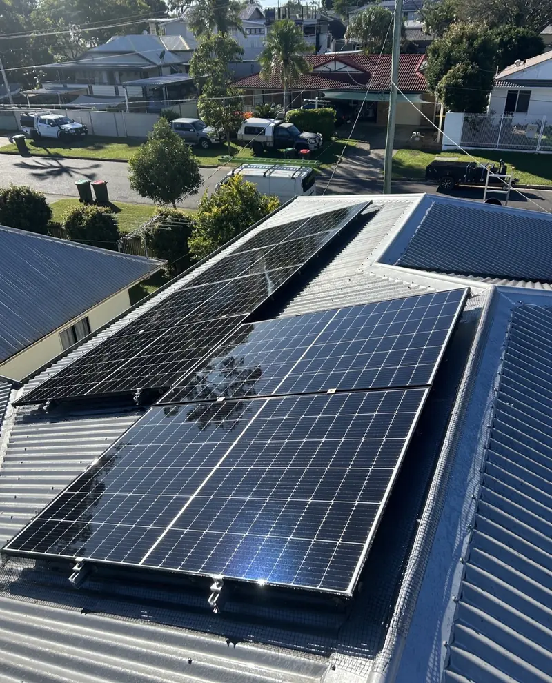 Solar panel bird proofing in Shailer Park: Black solar panels with mesh skirting on a dark grey corrugated metal roof above a suburban street