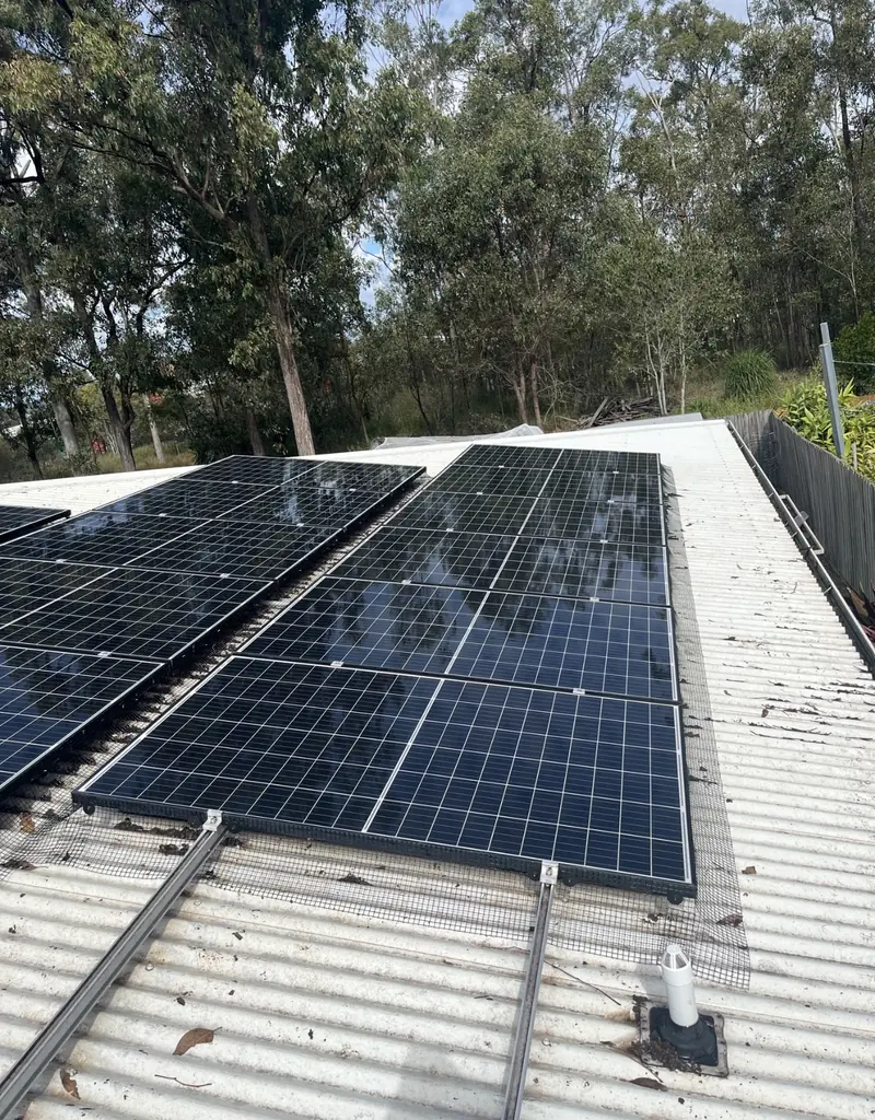 Solar panel bird proofing in Springfield Lakes: Blue solar panels with mesh skirting on a white corrugated metal roof surrounded by gum trees