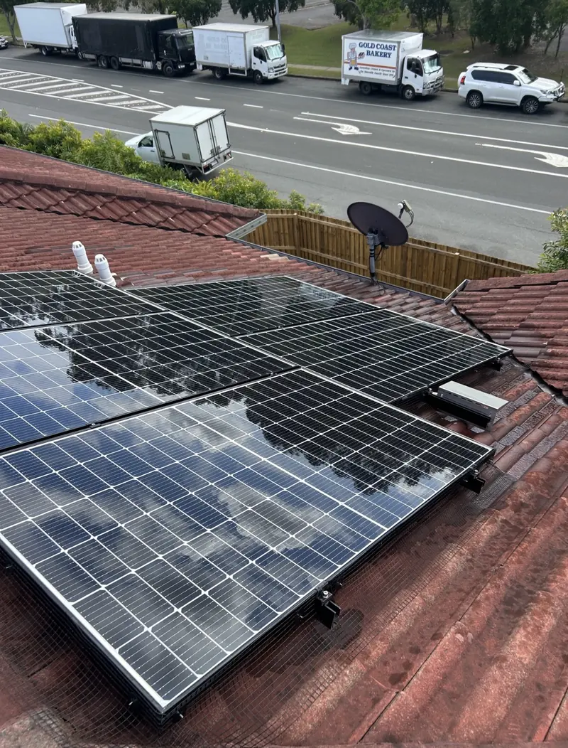 Solar panel bird proofing in Springwood: Black solar panels with edge mesh on a weathered red tile roof beside a busy road