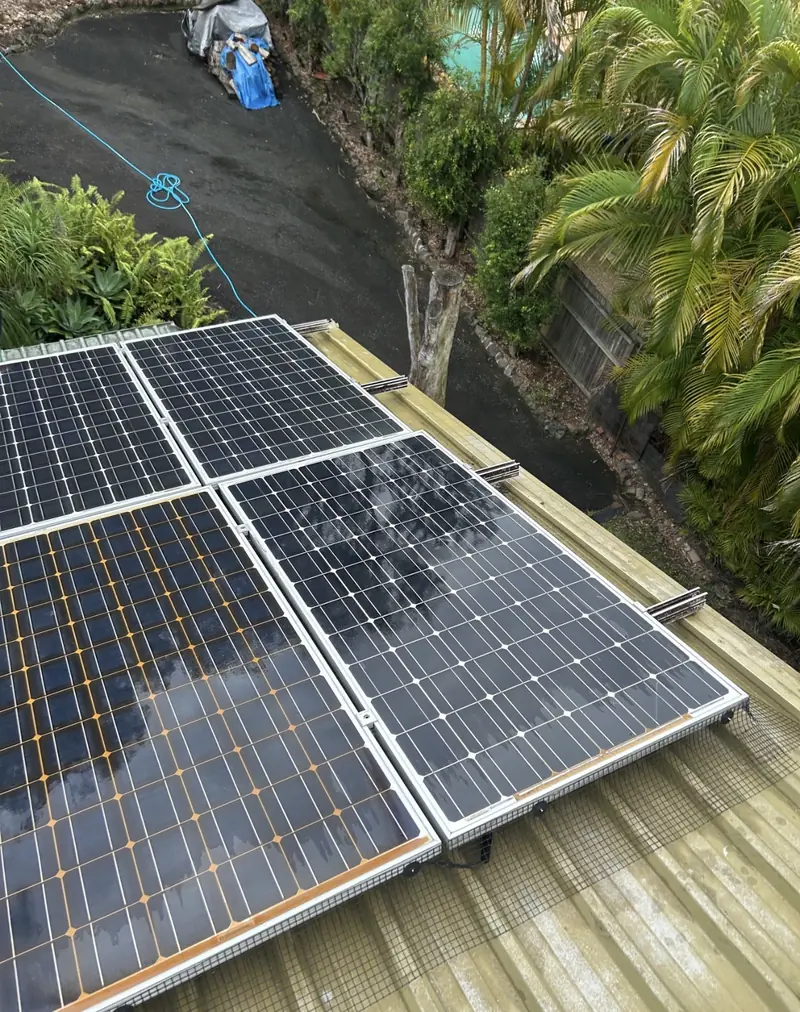 Solar panel bird proofing in Stafford: Wet solar panels edged with black mesh on a pale green metal roof above a driveway